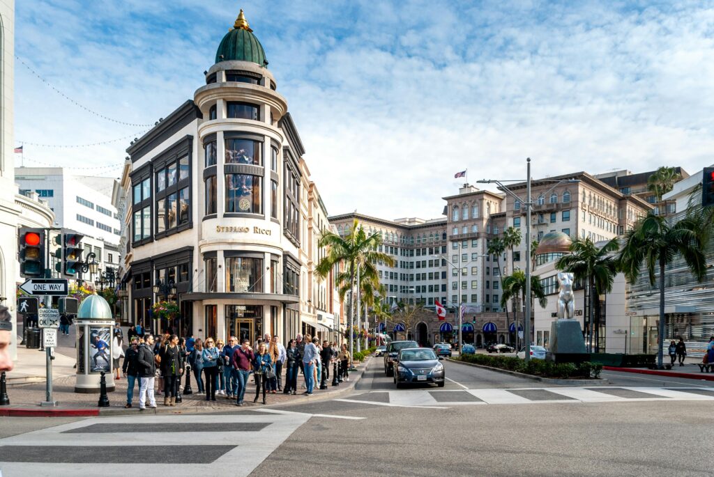 A vibrant street scene on Rodeo Drive in Beverly Hills, featuring luxury storefronts, palm trees, and bustling shoppers enjoying a sunny day.