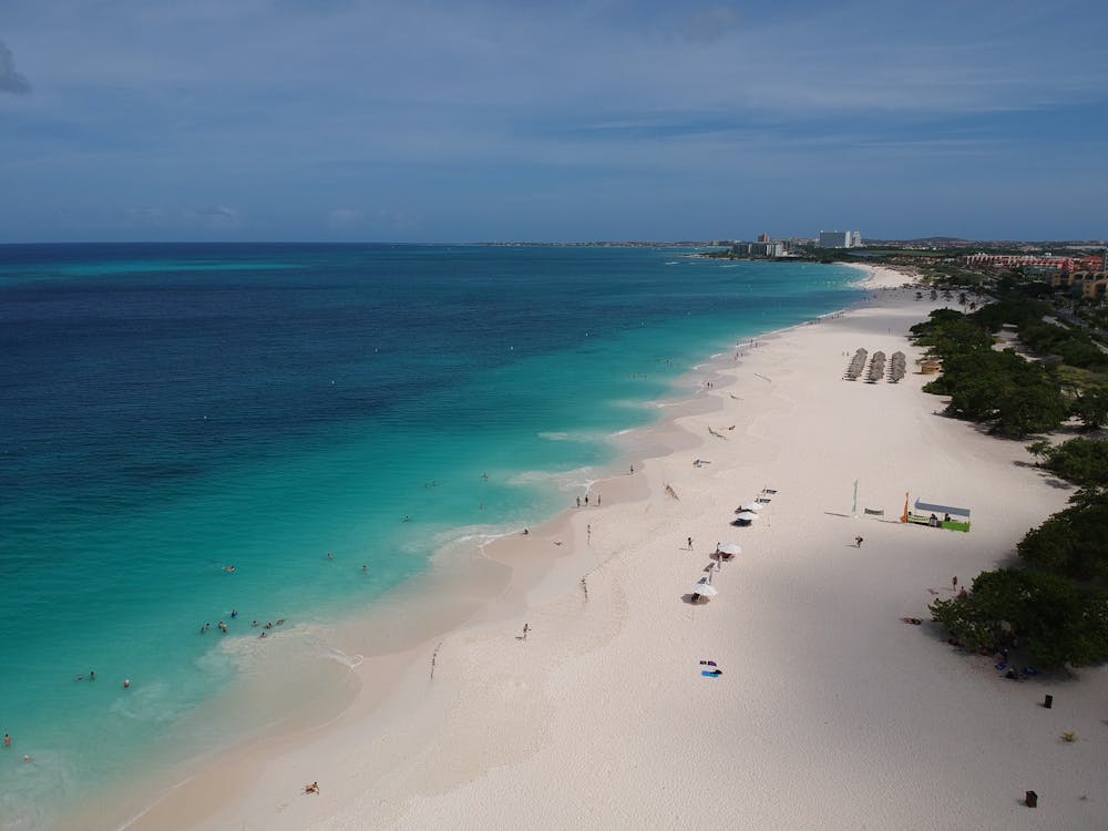 A stunning aerial view of a white sandy beach in Aruba, with turquoise waters and beachfront resorts in the distance.