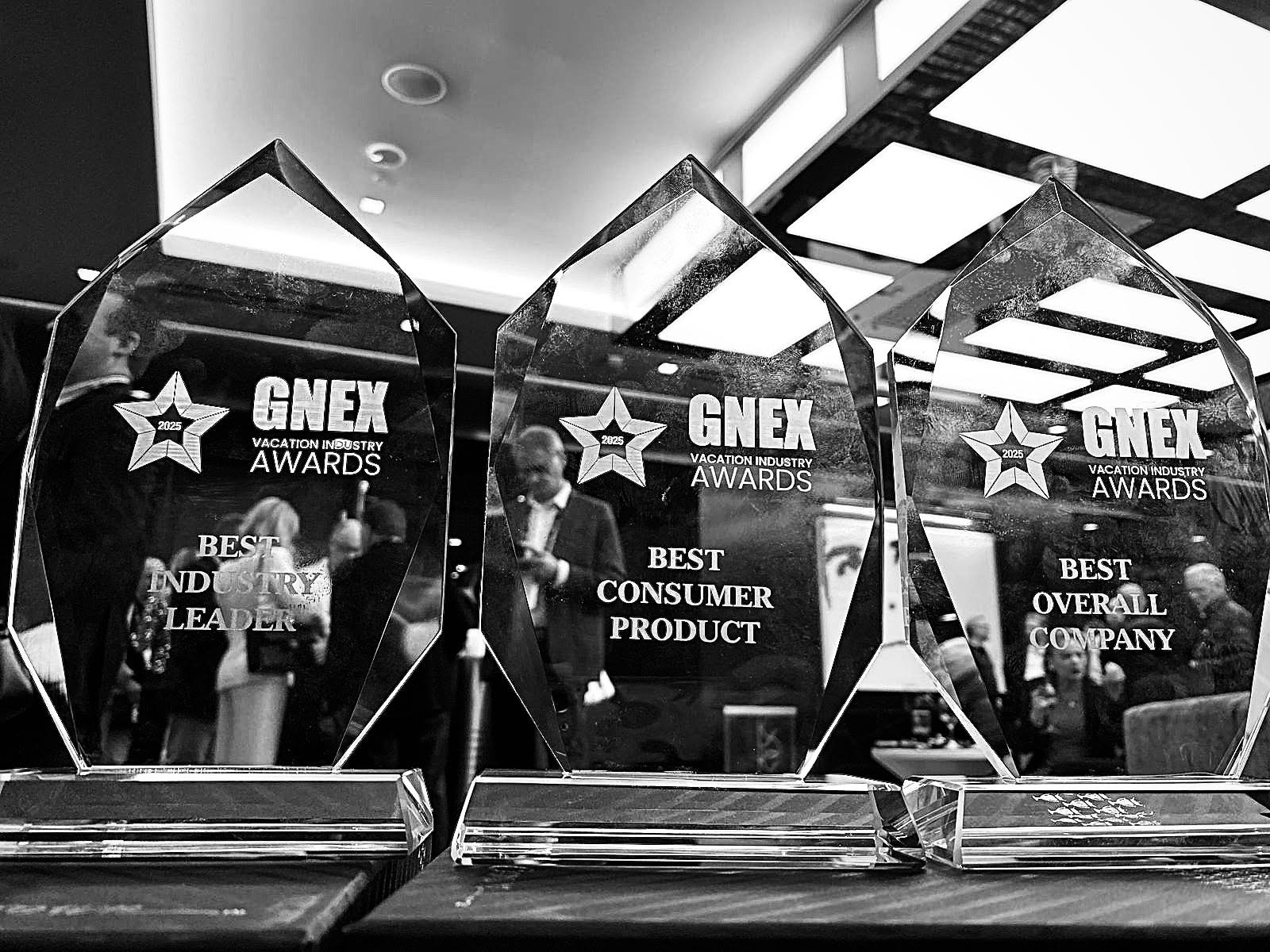A close-up black-and-white image of three GNEX Vacation Industry Awards trophies displayed on a table. The awards recognize Best Industry Leader, Best Consumer Product, and Best Overall Company, reflecting excellence in the vacation ownership industry.