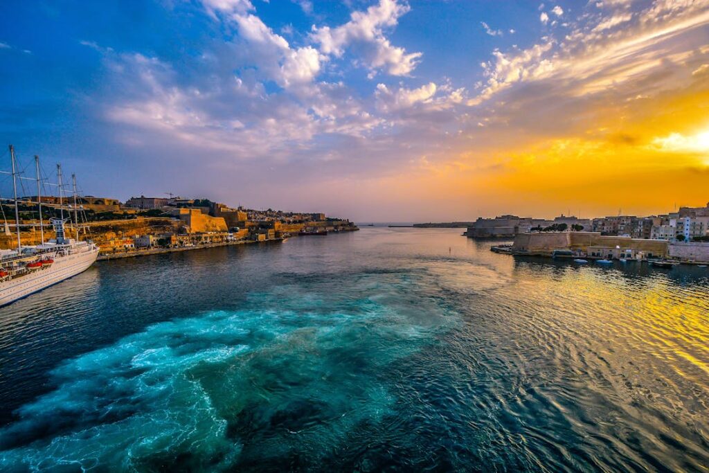 A stunning sunset over the Mediterranean Sea in Valletta, Malta, with a luxury cruise ship docked near the historic fortifications.