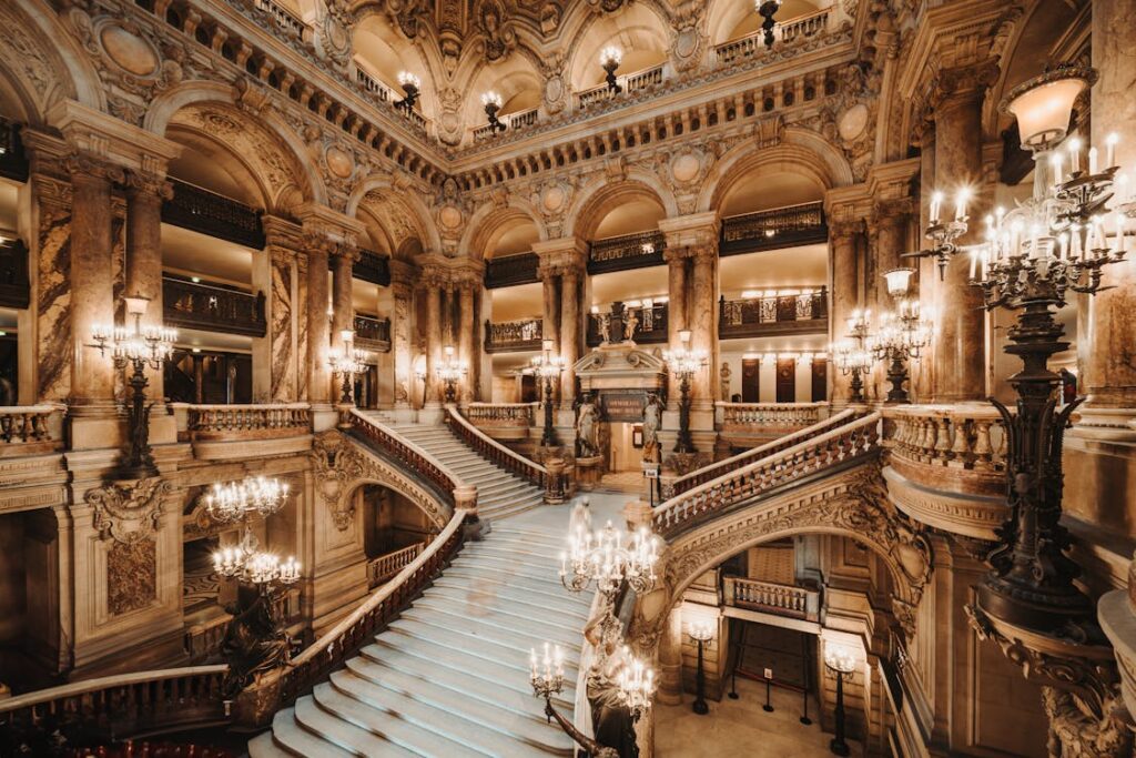 A grand staircase inside the opulent Palais Garnier in Paris, illuminated by elegant chandeliers, showcasing intricate architecture and luxury
