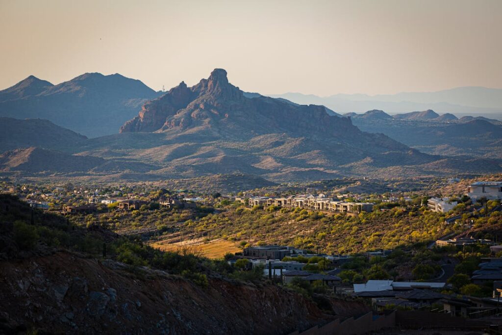 A scenic view of the Arizona desert landscape near Scottsdale, featuring rugged mountains, lush greenery, and luxury homes nestled in the valley under a warm golden sunset.