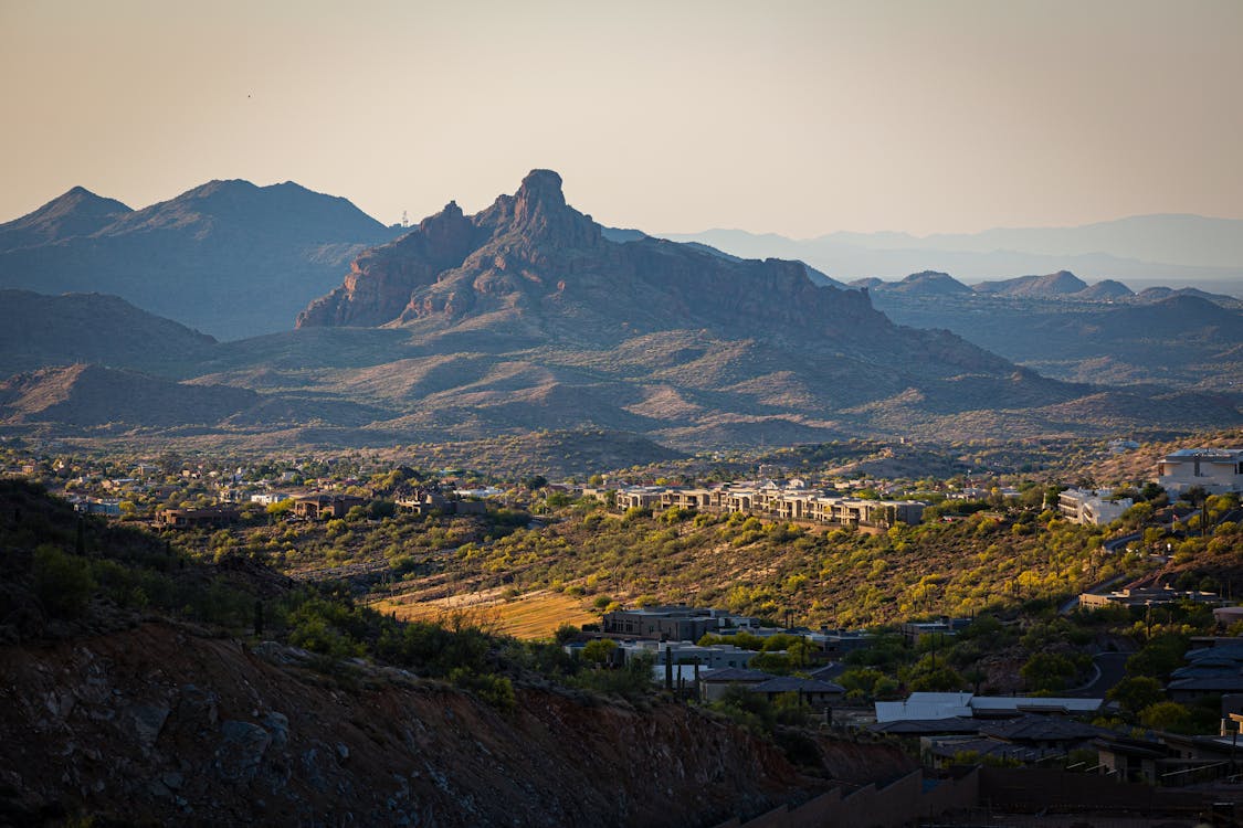 A scenic view of the Arizona desert landscape near Scottsdale, featuring rugged mountains, lush greenery, and luxury homes nestled in the valley under a warm golden sunset.
