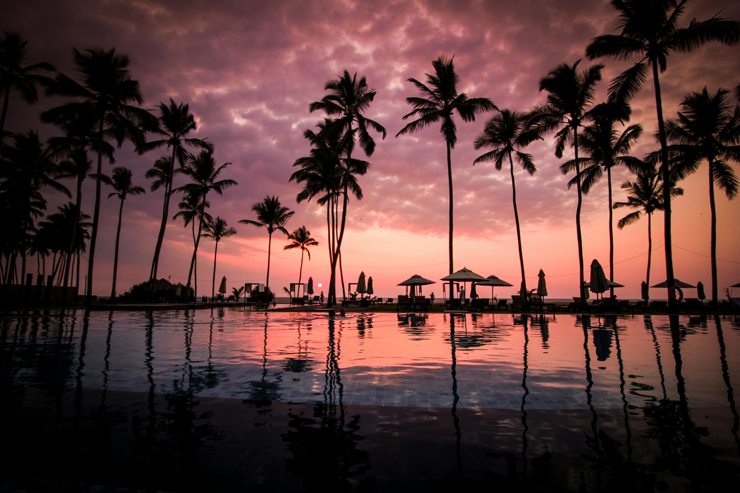 Stunning sunset over a luxury resort pool lined with palm trees, creating a serene and tropical atmosphere.