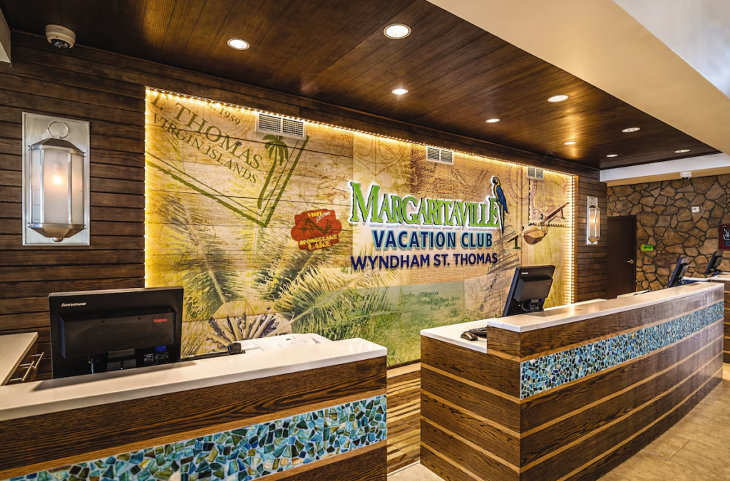 Reception area of Margaritaville Vacation Club – Wyndham St. Thomas, featuring a tropical-themed illuminated wall with a large resort logo, wooden counters with mosaic tile accents, and a welcoming island ambiance.