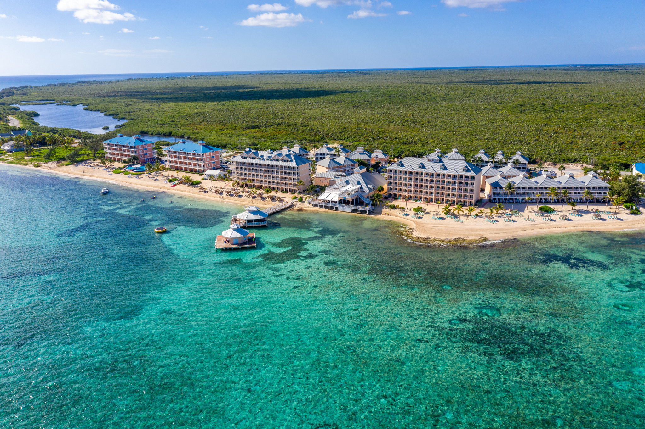 Aerial view of Morritt’s Tortuga Club resort in Grand Cayman, featuring beachfront suites, turquoise waters, and private dock areas.