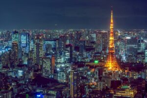 Tokyo skyline at night with Tokyo Tower illuminated in vibrant orange, surrounded by city lights and modern skyscrapers.