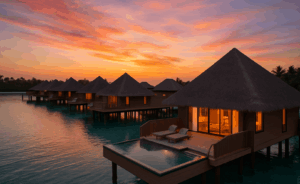 Overwater villas with thatched roofs in the Maldives, glowing with warm interior lights at sunset, overlooking turquoise water with a private plunge pool.