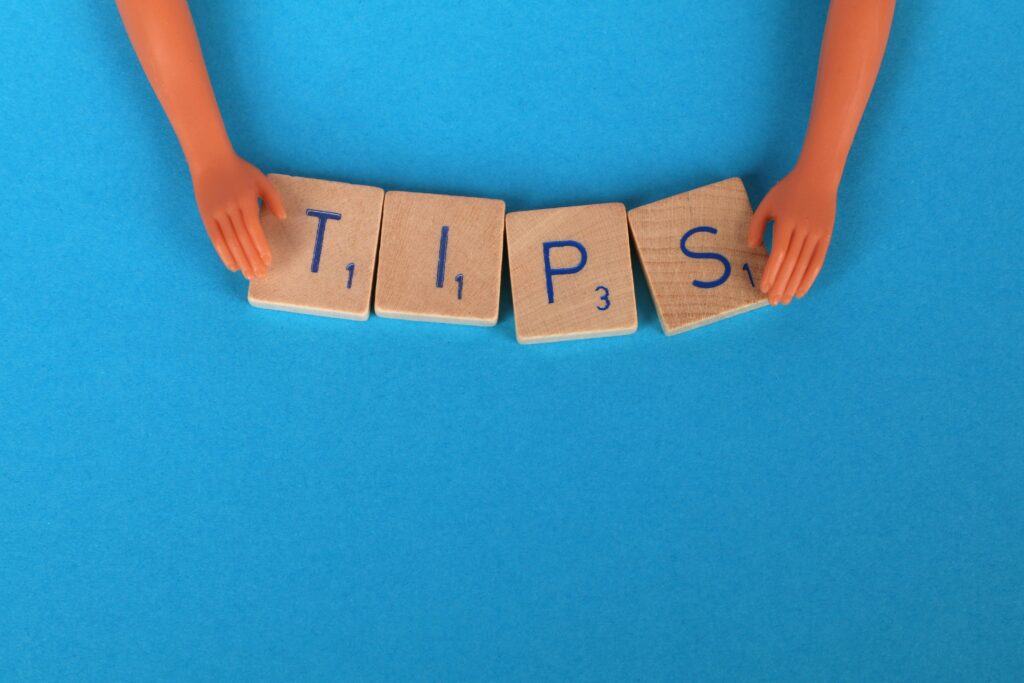 Plastic hands holding wooden tiles spelling “TIPS” on a blue background.