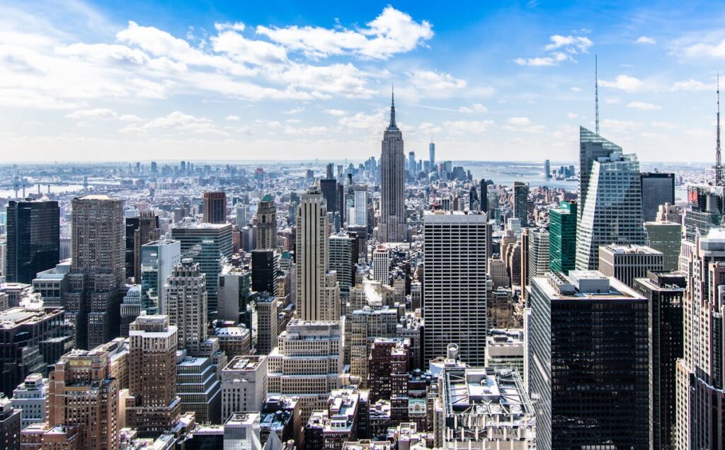 Panoramic view of Midtown Manhattan with the Empire State Building and Hudson River under a blue sky.