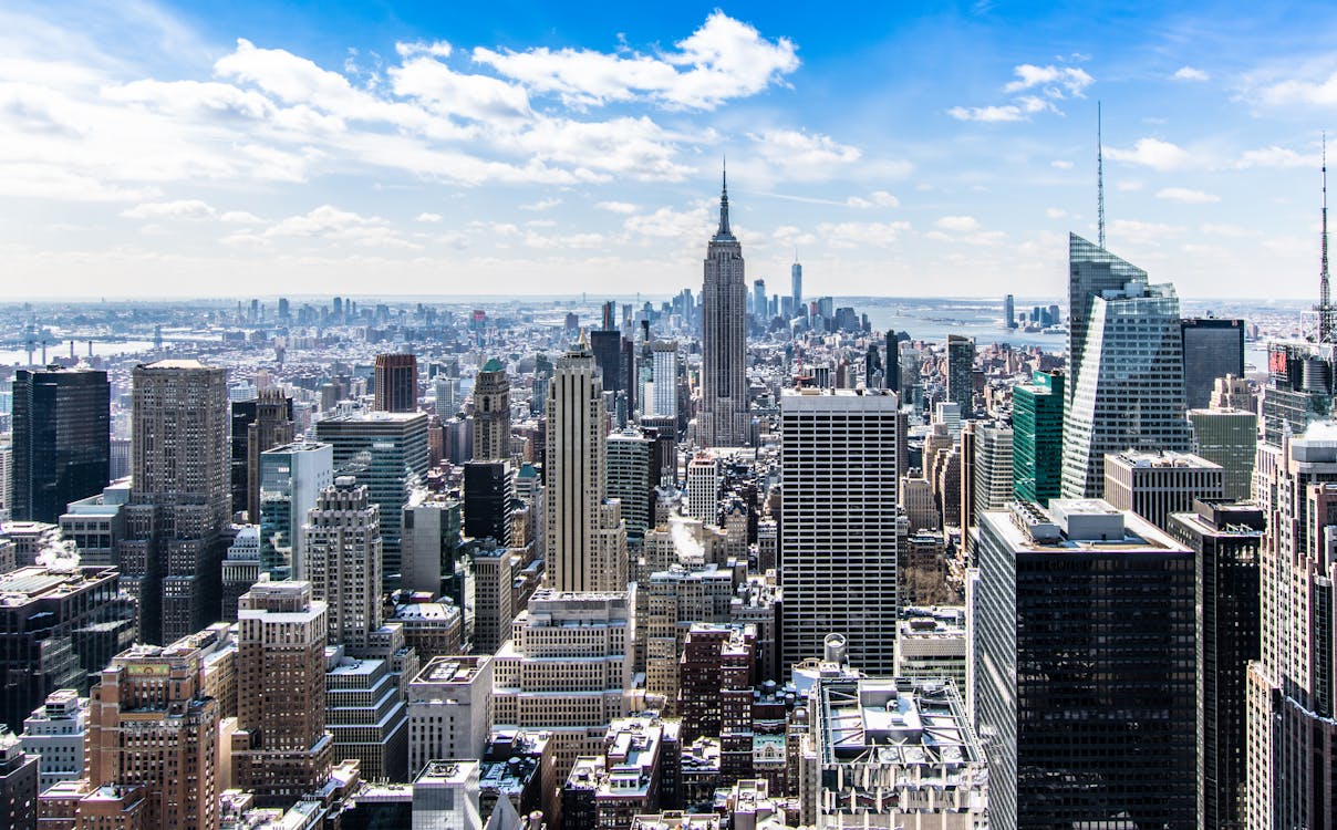 Panoramic view of Midtown Manhattan with the Empire State Building and Hudson River under a blue sky.