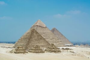 The Great Pyramids of Giza standing tall under a clear blue sky, with the modern Cairo skyline faintly visible in the background.