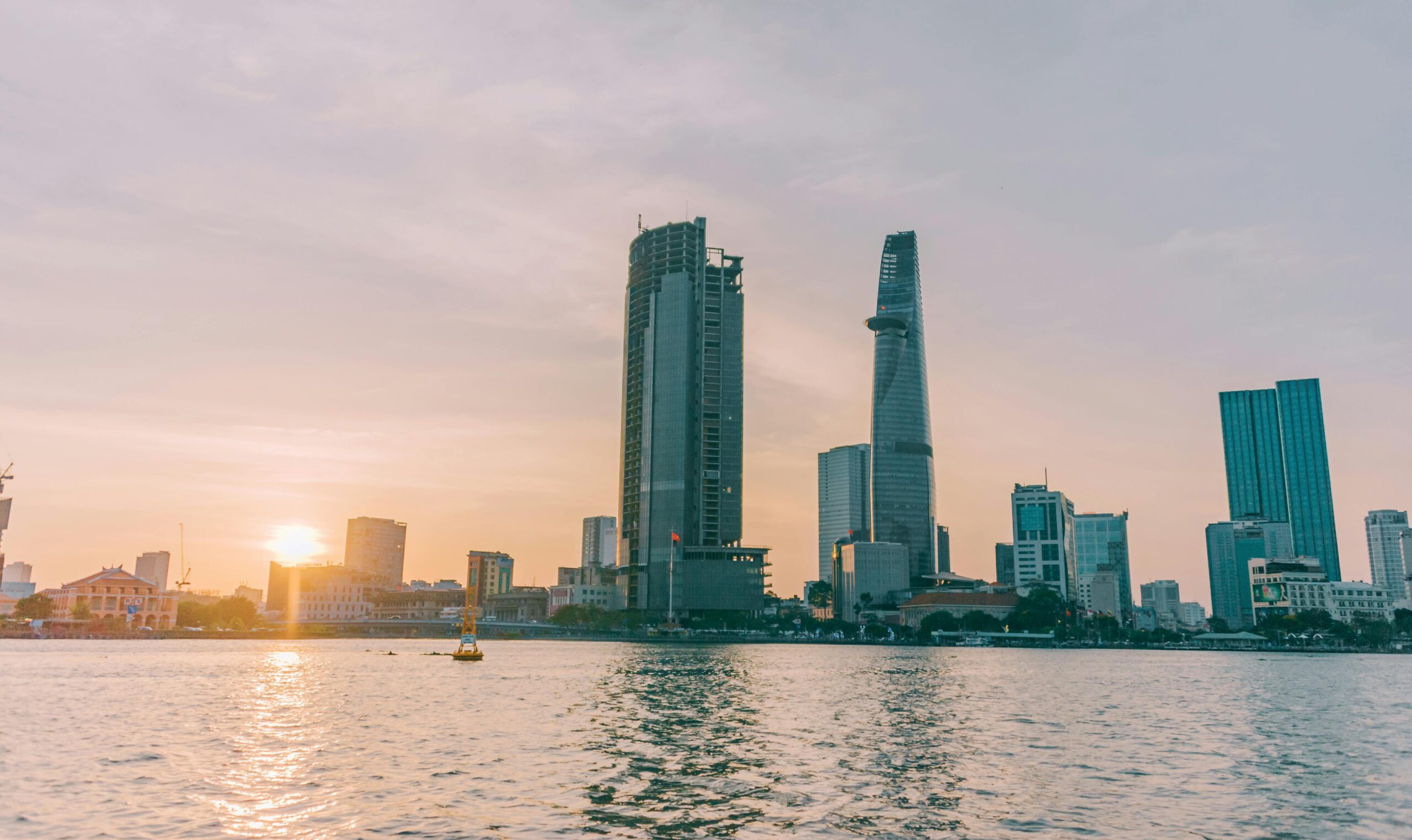 Skyline of Ho Chi Minh City at sunset with the Bitexco Financial Tower and nearby skyscrapers reflecting over the Saigon River.