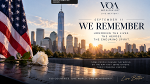 A white rose rests on the 9/11 Memorial with the American flag and One World Trade Center at sunrise, honoring the victims, first responders, and enduring spirit of September 11. The image features the message "We Remember" from VOA Worldwide®.